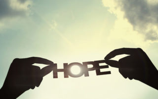 hands holding out the word hope in the sky.