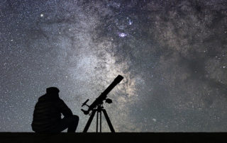 Silhouette of man with a telescope looking into the night sky at the stars.