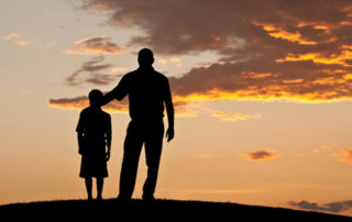 Silhouette of a father and his son standing and looking into the sky.