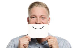 A man standing with a paper drawing of a smile in on his face.