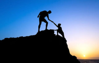 Silhouette of man helping a woman up the mountain.