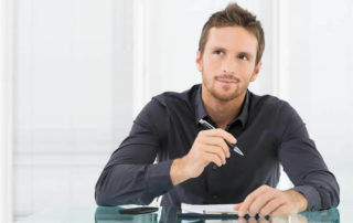 A man in blue shirt holding a pen and thinking what to write.