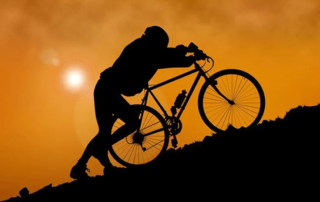 Silhouette of a man pushing his bicycle up the mountain.