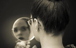 Woman with glasses looking at herself in the mirror.