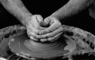 Hands mending clay to a form of a pot.