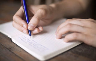 A man writing in a journal with a blue pen.