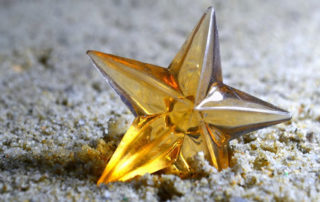 A closeup of a bright yellow glass looking star on sand.