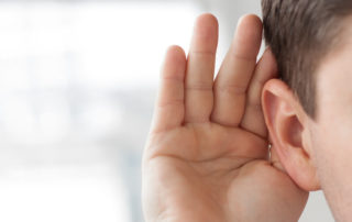 A man's hand behind his ear listening.