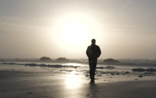 Silhouette of man walking towards the sun on the beach.