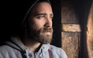 A man with a beard looking out a window.