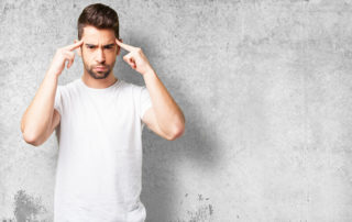 man with white t-shirt thinking with his fingers pointing to his head.